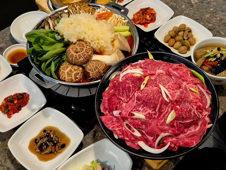 한우얼큰전골 한상. 얼큰한 육수의 전골이 밑반찬과 함께 차려져 있다.